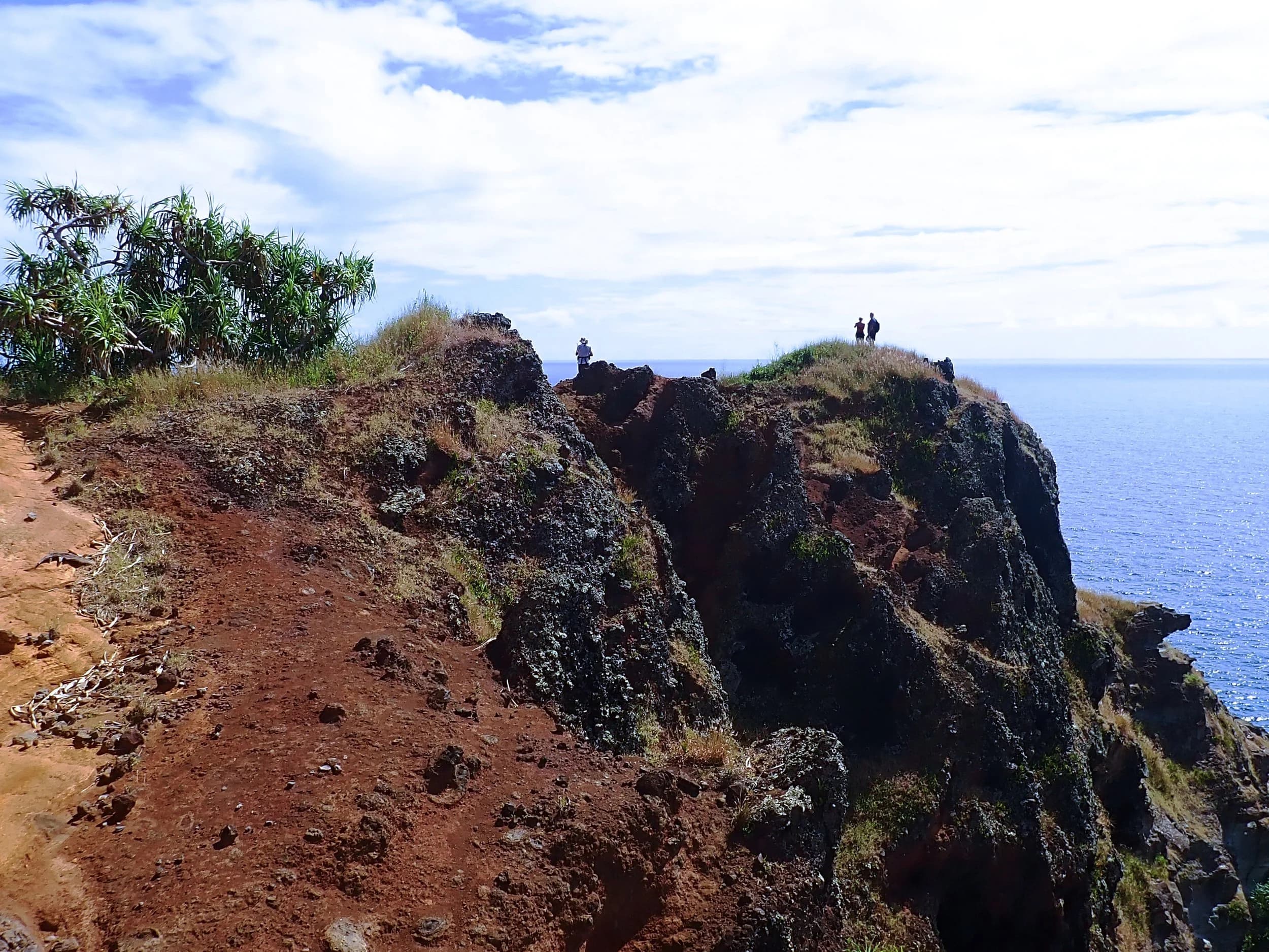 Red earth cliffs and green bush high above the sea, two walkers on the top