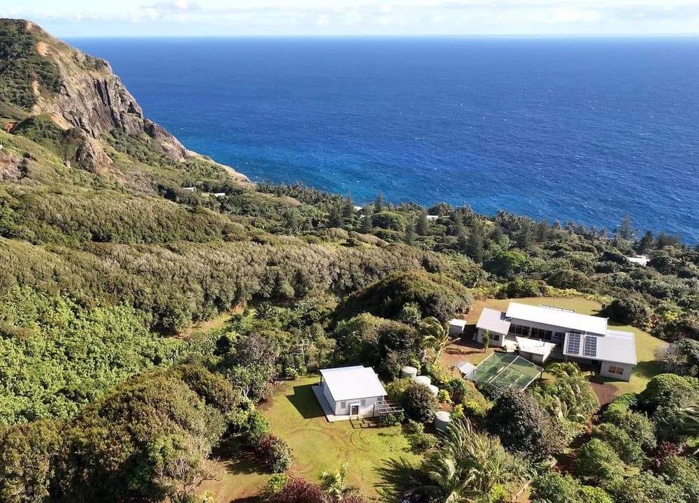 Aerial view of a coastal house surrounded by lush greenery near a cliff and ocean